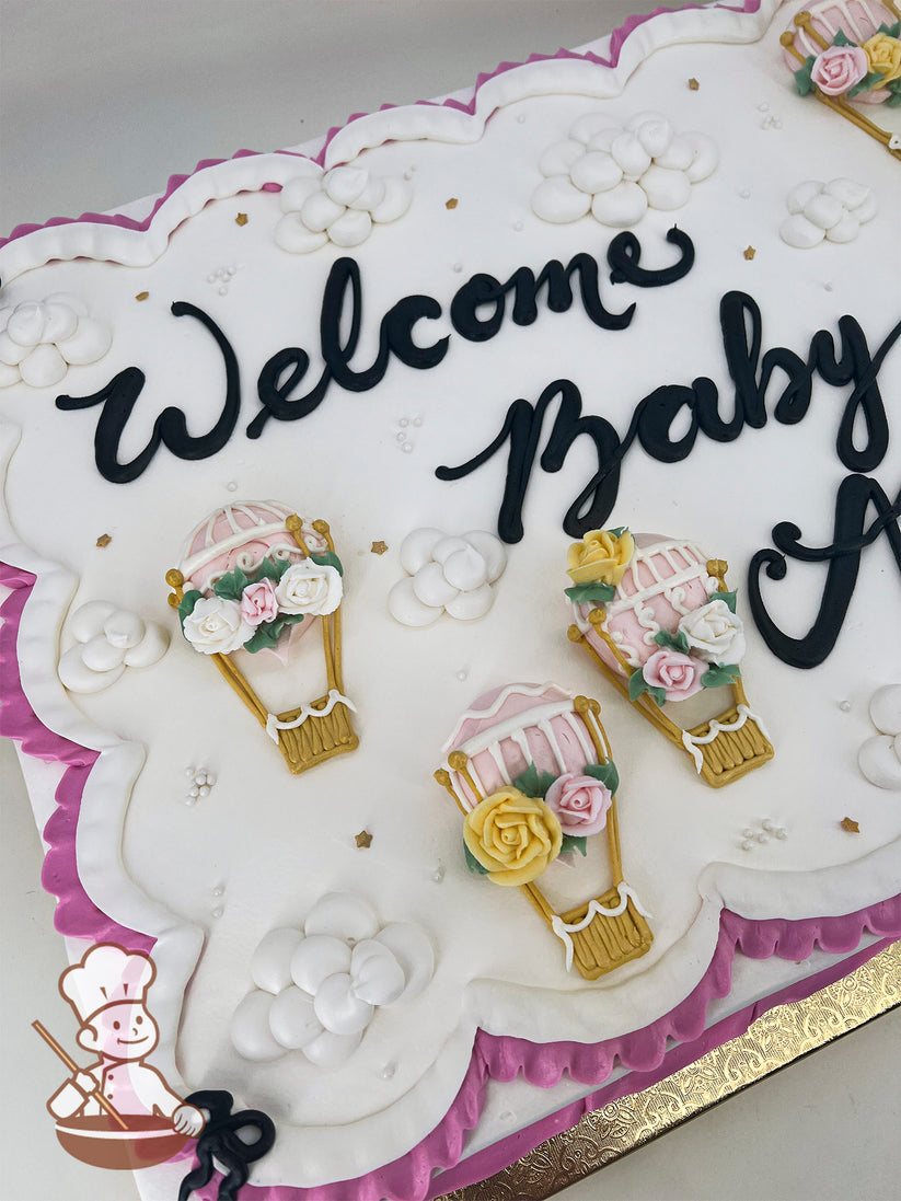 White sheet cake with pink scalloped edges, decorated with buttercream hot air balloons, pastel roses, white clouds, and small gold star accents.