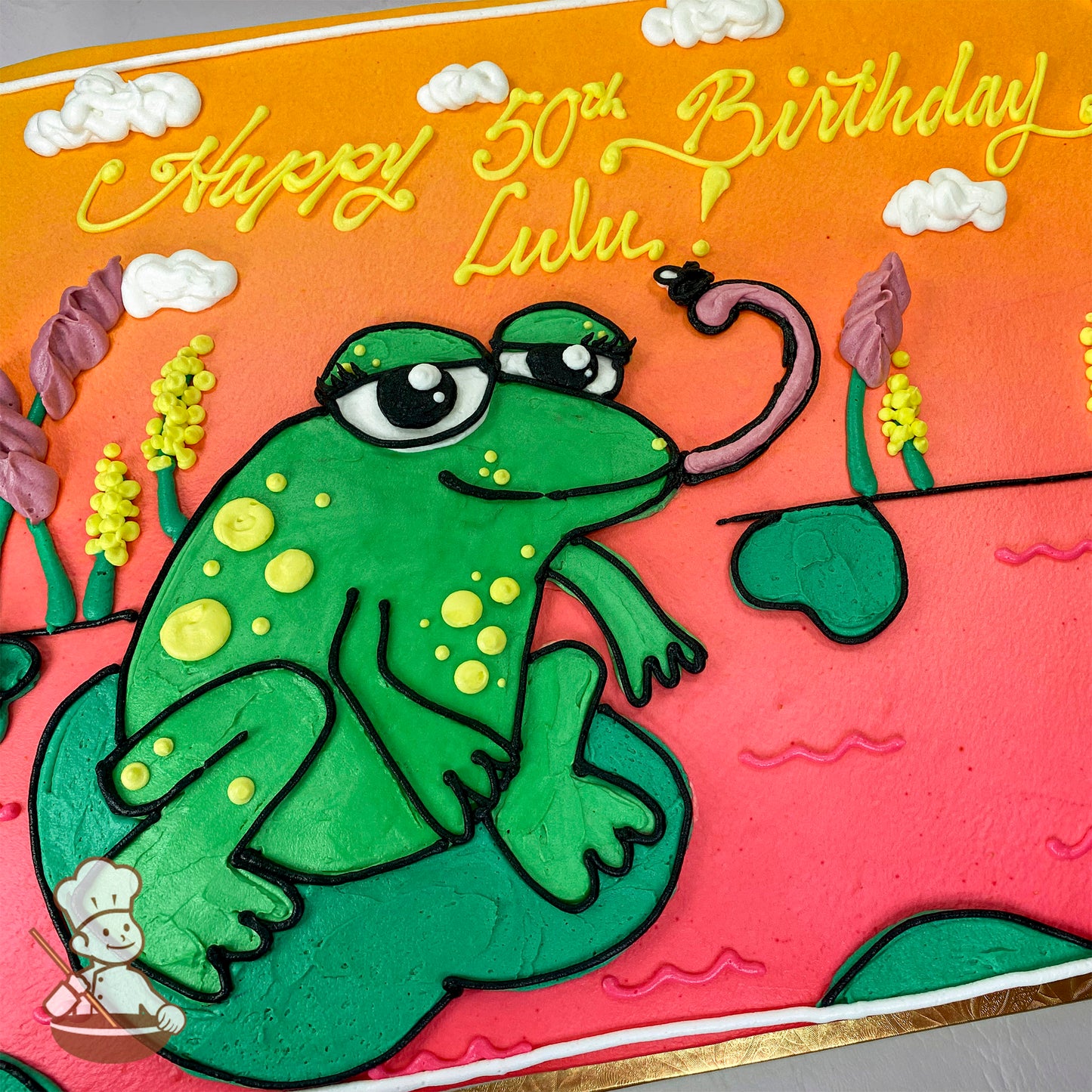 A sheet cake with a green buttercream frog sitting on a lily pad, surrounded by flowers and clouds, on a vibrant orange and pink background.