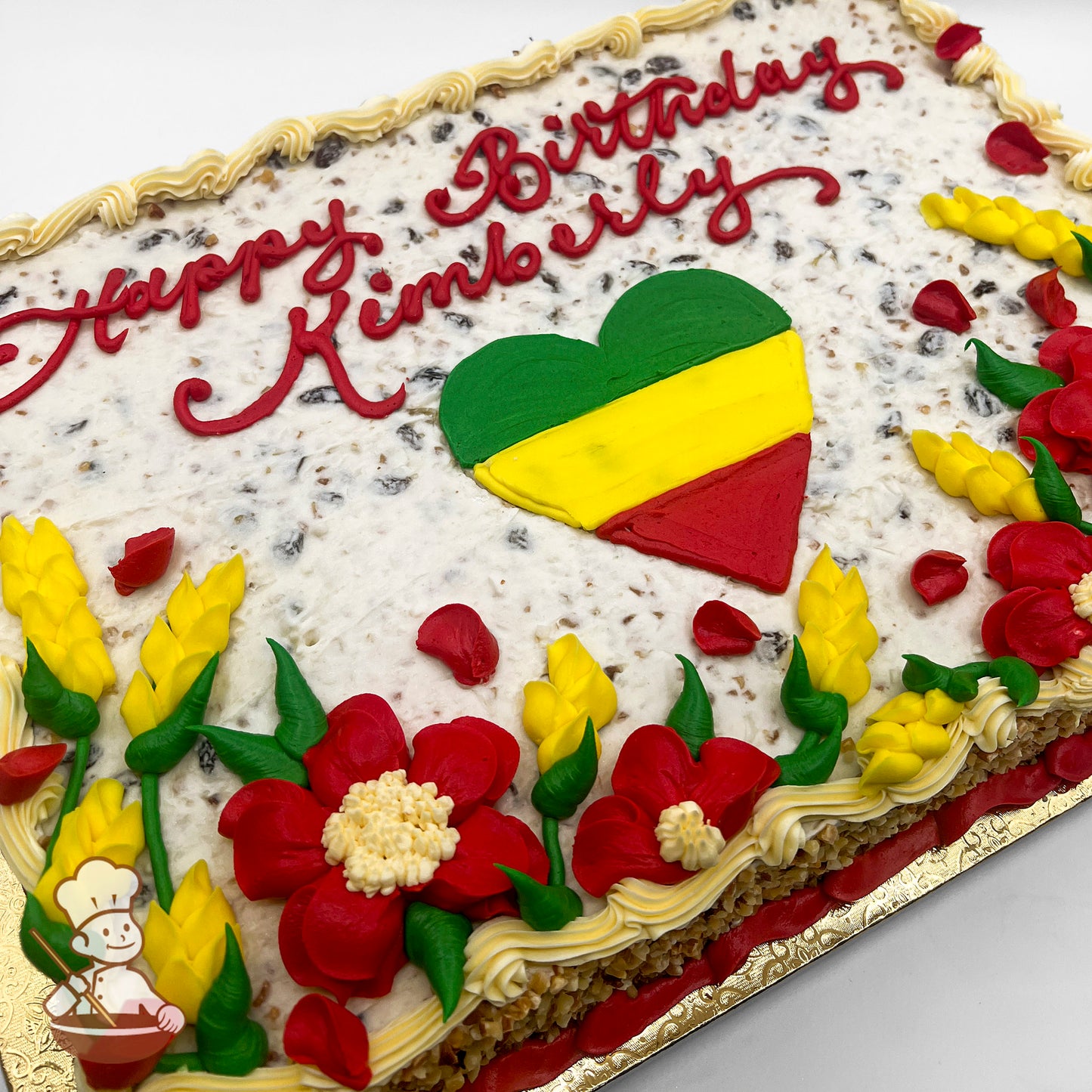 Sheet cake with a heart in green, yellow, and red icing, surrounded by red and yellow buttercream flowers, green leaves, and piped borders.