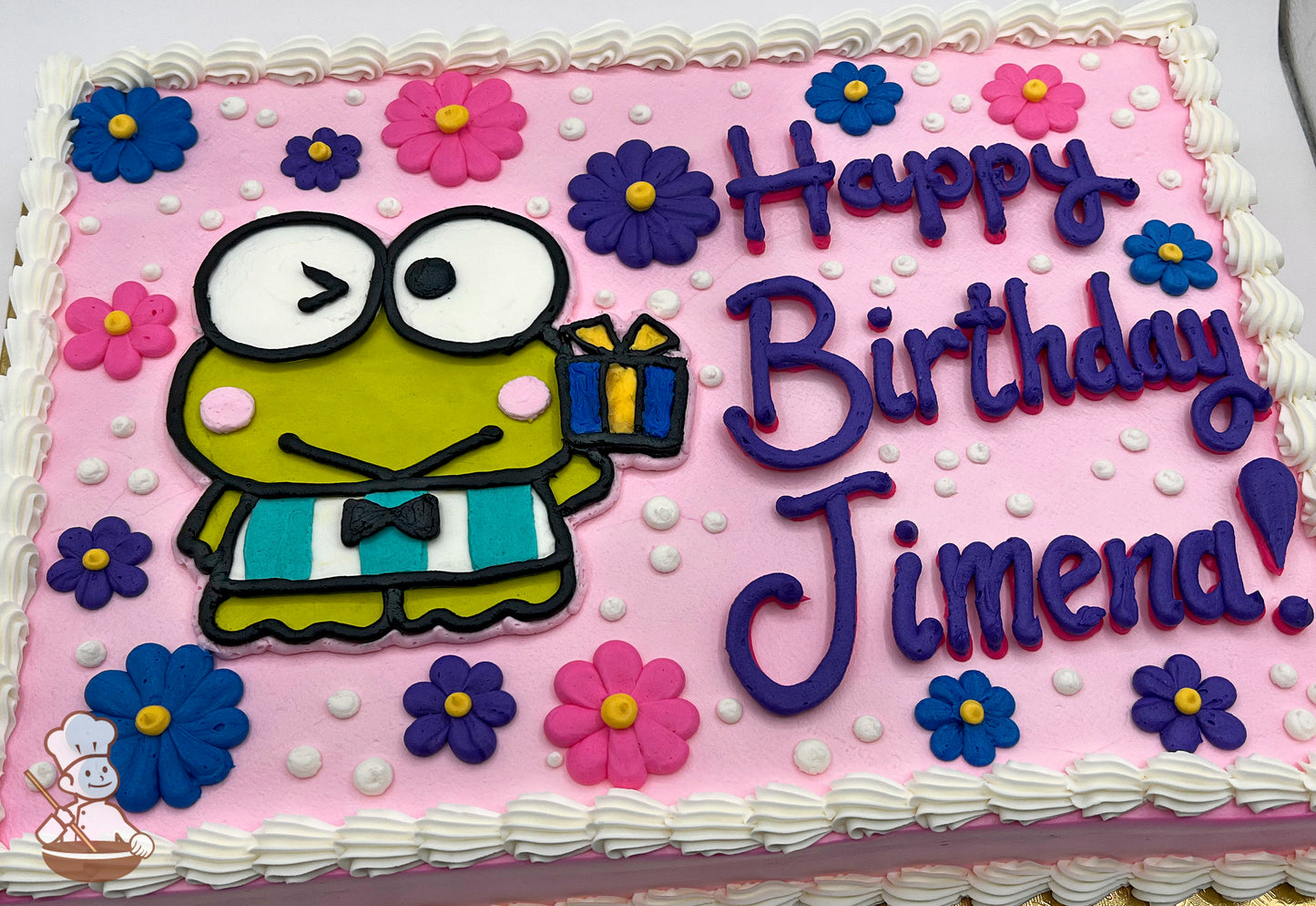 Kerokerokeroppi character in buttercream on a pink sheet cake, surrounded by colorful buttercream flowers and white dots, with a white piped border.