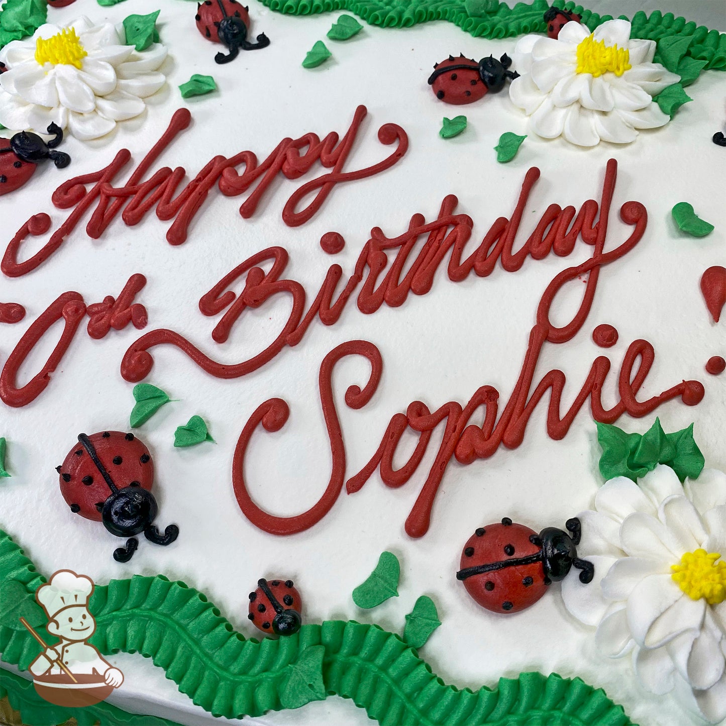 Sheet cake with white frosting, decorated with red ladybugs, white and yellow blossom flowers, green leaves, and piped green borders.