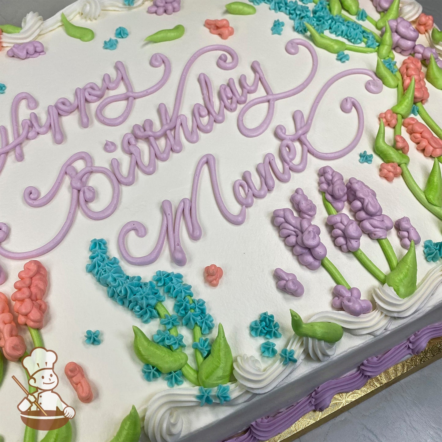 Sheet cake with white frosting, decorated with lavender and lupine flowers in purple, pink, and blue, with green stems and leaves.