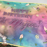 Sheet cake with a pastel gradient background of pink, purple, and blue, decorated with buttercream lavender flowers, small yellow blossoms, and green leaves.