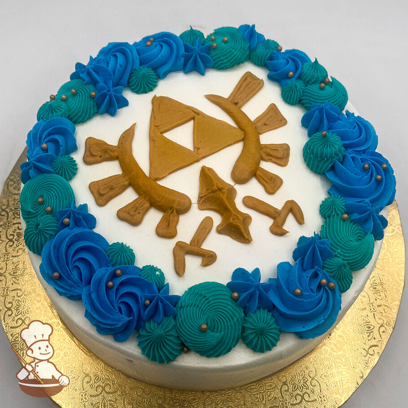 Round cake with white frosting, decorated with a gold Triforce symbol and Sheikah Eye design. Blue and teal buttercream swirls and stars with gold pearl accents form a border.