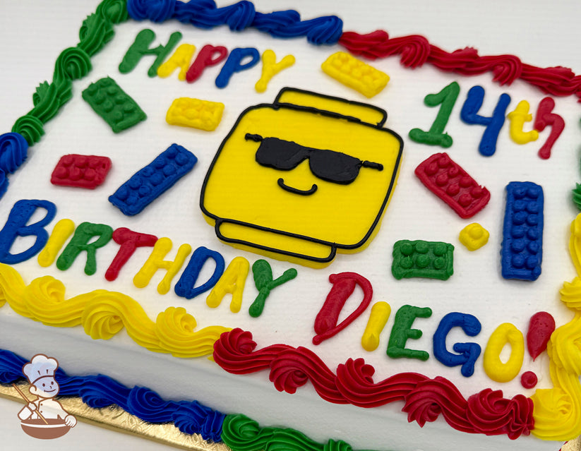 Sheet cake with colorful buttercream decorations, featuring a yellow Lego head with sunglasses, surrounded by red, blue, green, and yellow Lego brick designs.