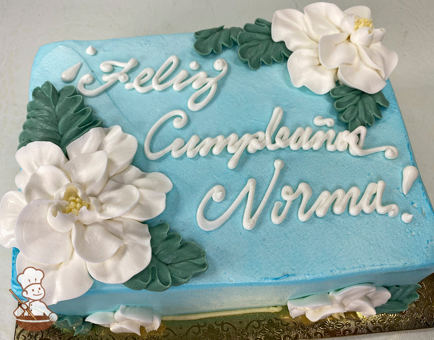 Light blue sheet cake with white buttercream gardenia flowers and green leaves as decorations.