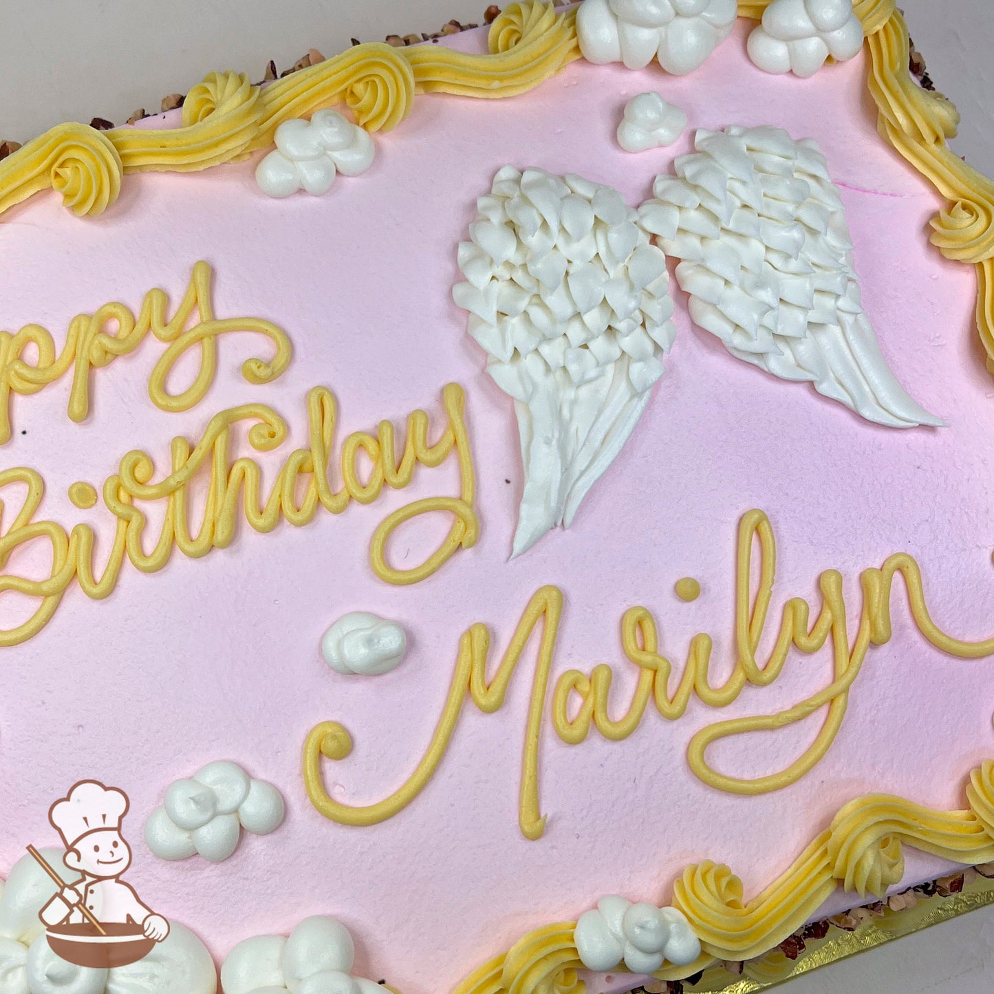 Pink sheet cake with white buttercream angel wings, small white clouds, and yellow buttercream borders.