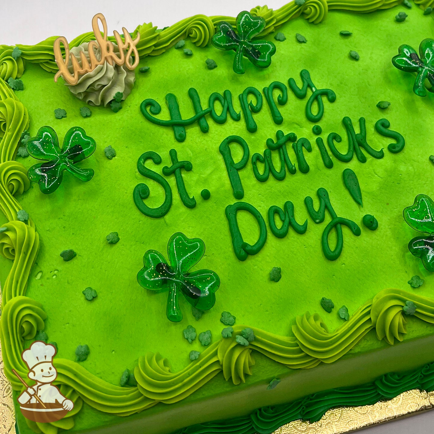 Green sheet cake with buttercream swirl trims, plastic shamrock rings, and shamrock sprinkles.