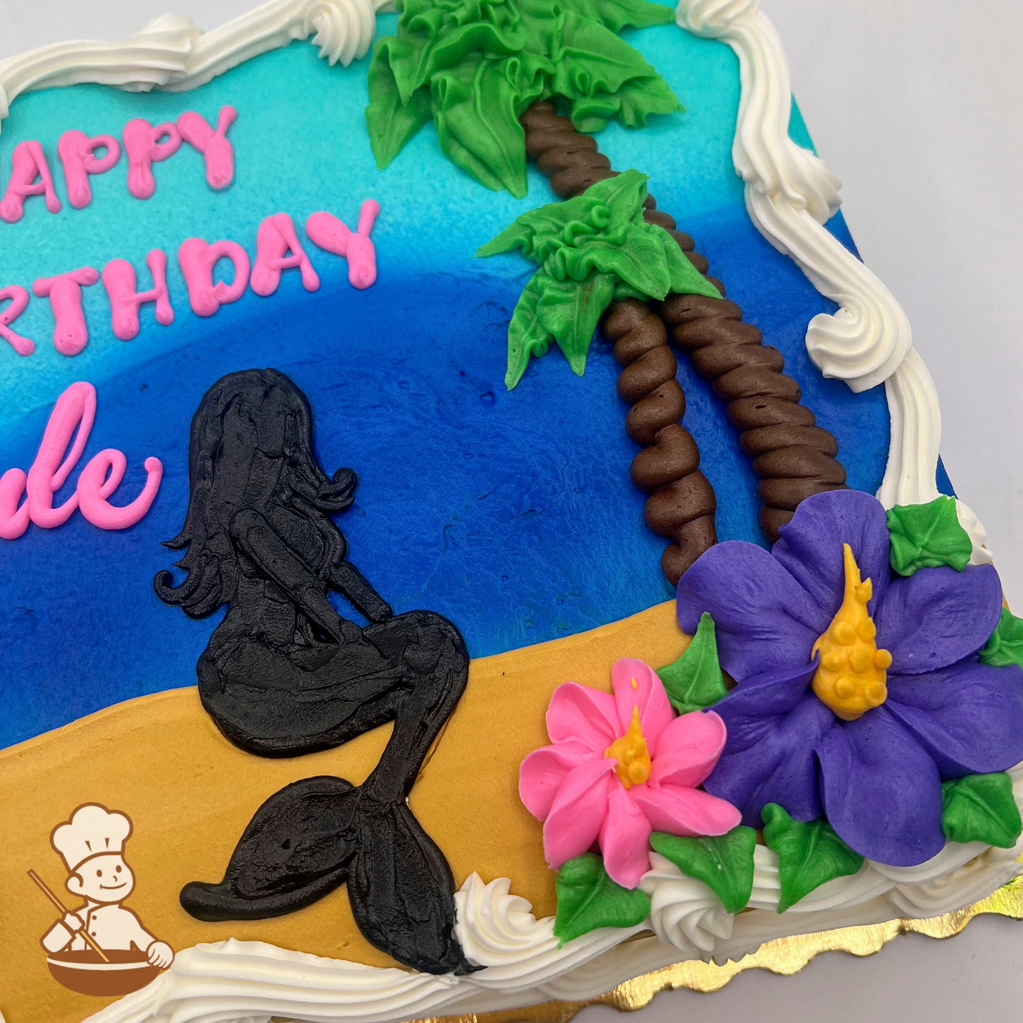 Sheet cake with buttercream decorations featuring a black mermaid silhouette on a sandy beach, blue ocean, palm trees, and pink and purple flowers.