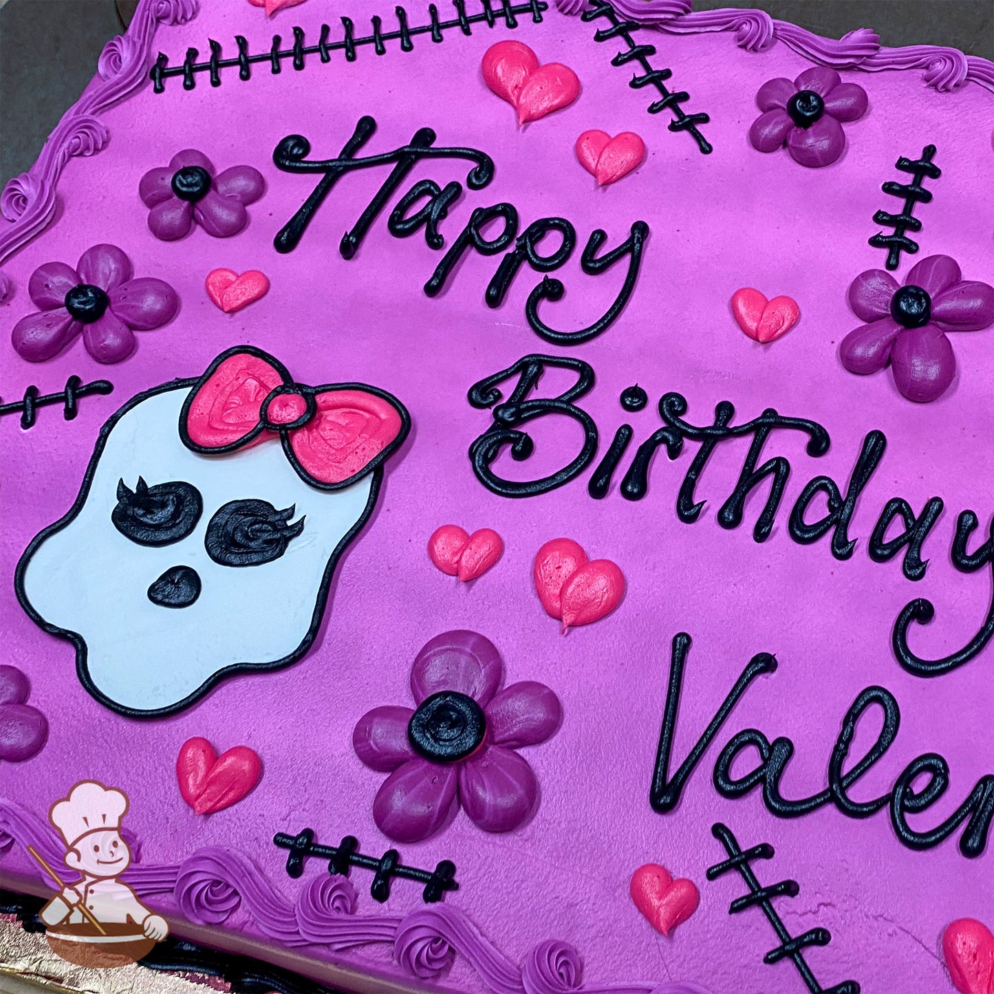 Purple sheet cake with buttercream decorations, including black stitches, pink hearts, purple flowers, and a Monster High skull with a pink bow.