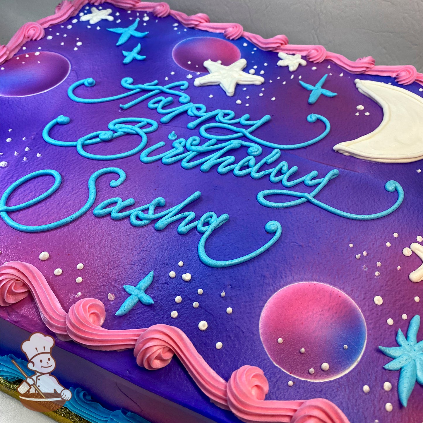 Sheet cake with a purple and pink galaxy design, featuring buttercream stars, a crescent moon, and a pink border. White dots resemble stars.