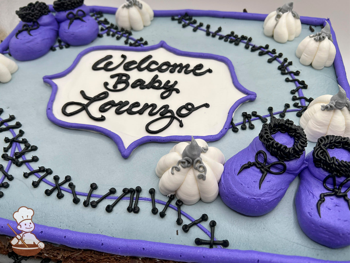 Sheet cake with light gray icing, purple border, black stitch designs, white pumpkins with gray stems, and purple baby booties with black laces.