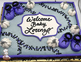 Sheet cake with light gray icing, purple border, black stitch designs, white pumpkins with gray stems, and purple baby booties with black laces.