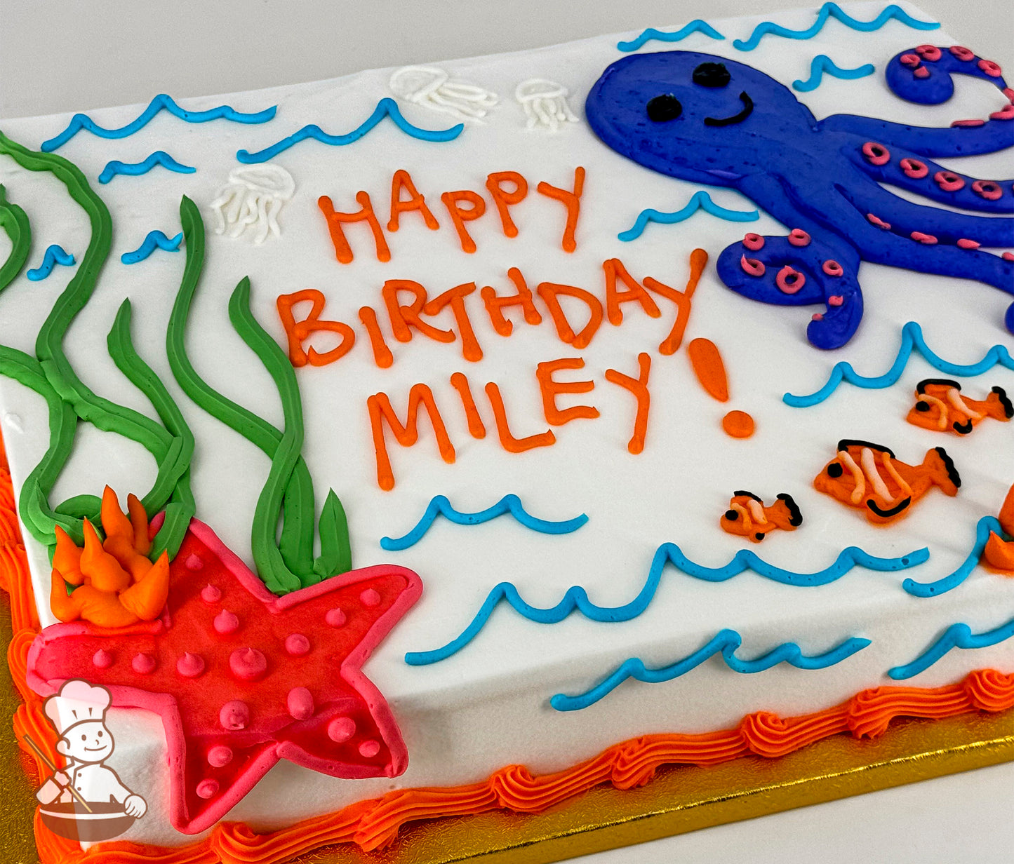 Sheet cake with white frosting, decorated with a blue octopus, red starfish, green seaweed, orange clownfish, blue waves, and white jellyfish.