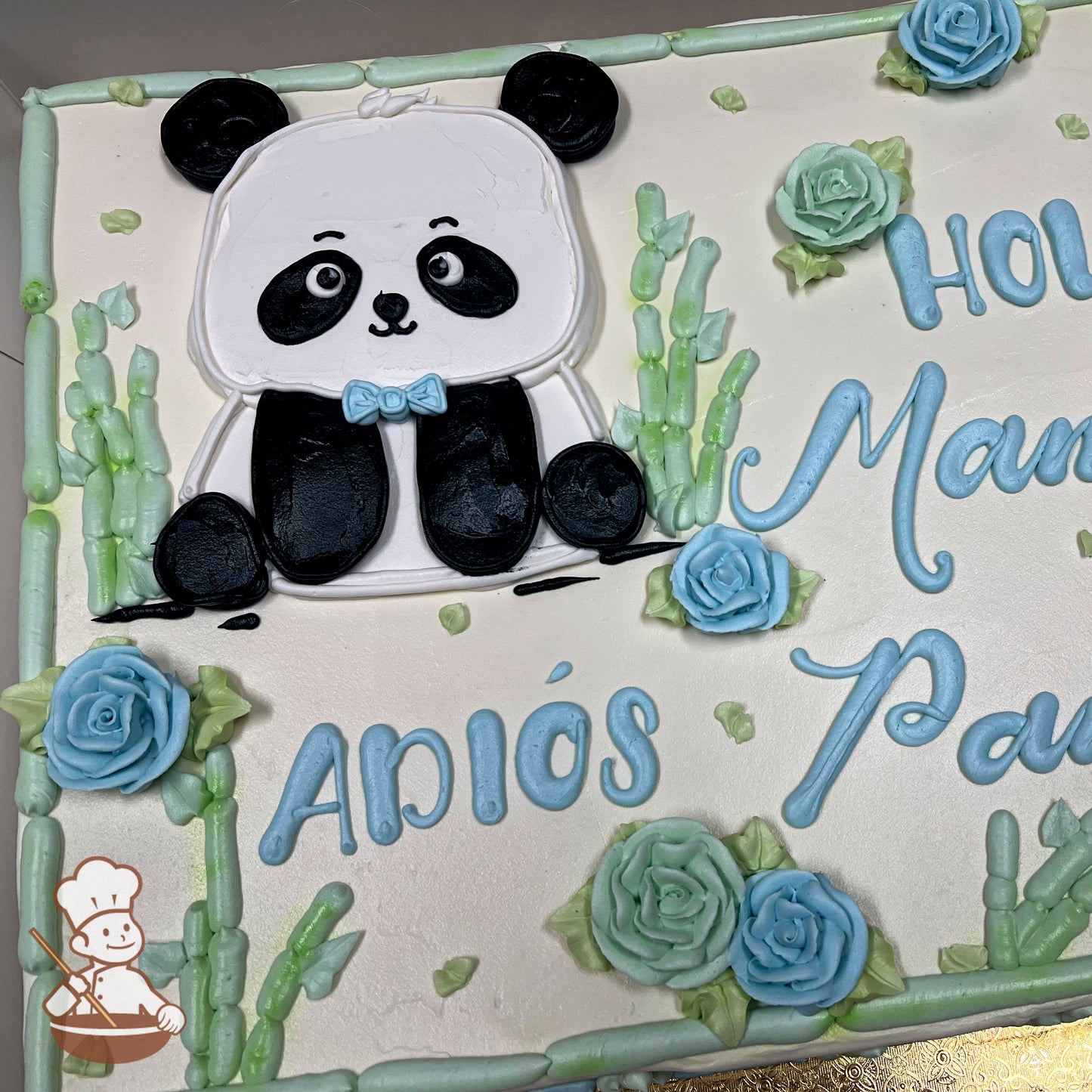 A sheet cake with a buttercream panda design wearing a blue bow tie, surrounded by green bamboo stalks and light blue buttercream roses.