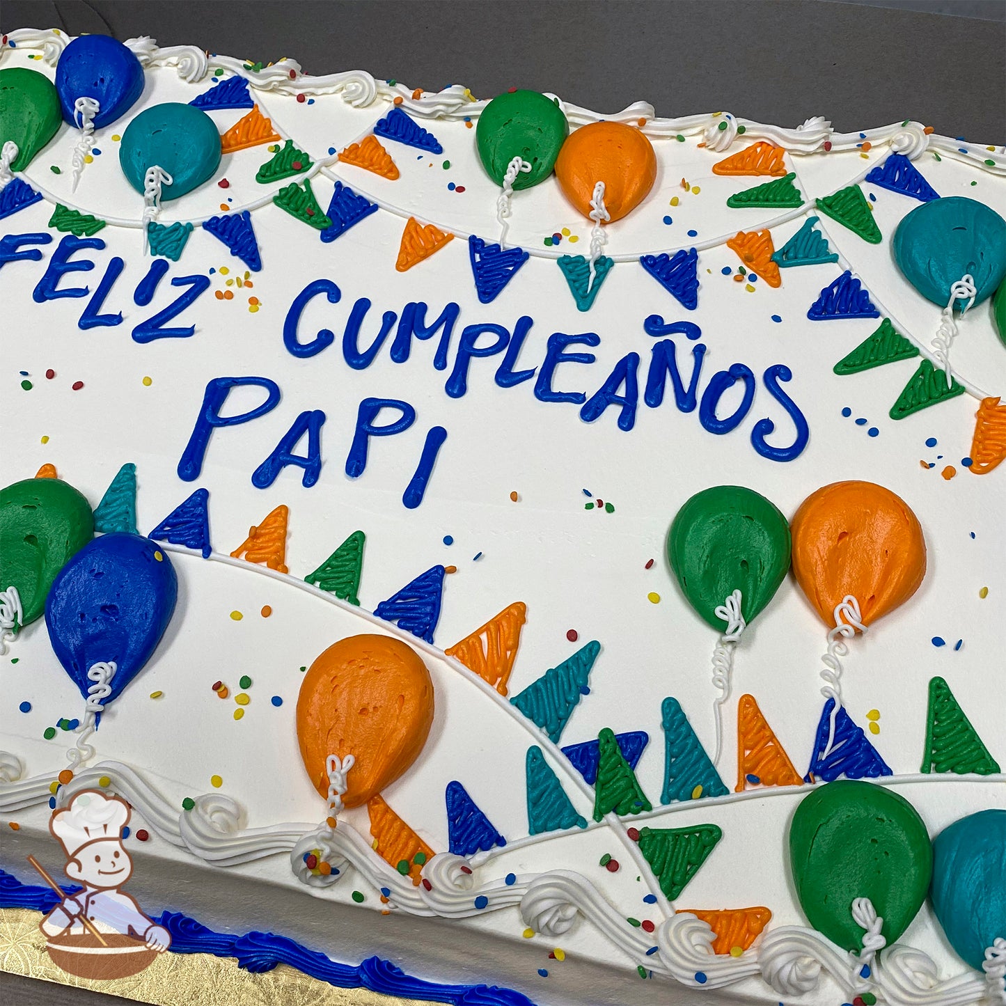 Sheet cake with white frosting, decorated with colorful balloons, triangular banners in green, blue, and orange, and scattered sprinkles.