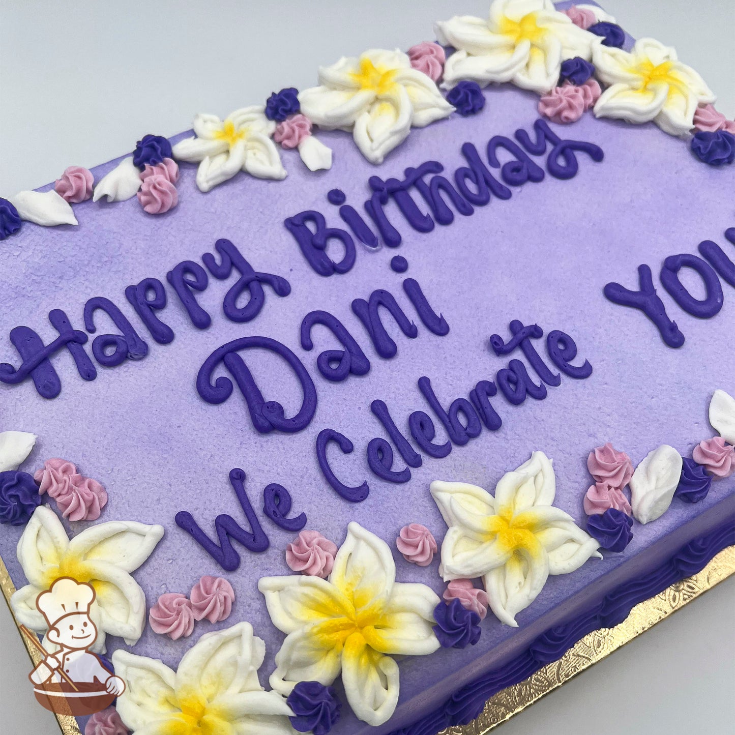 A purple sheet cake with buttercream plumeria flowers in white and yellow, accented by small pink and purple swirlette rosettes along the edges.