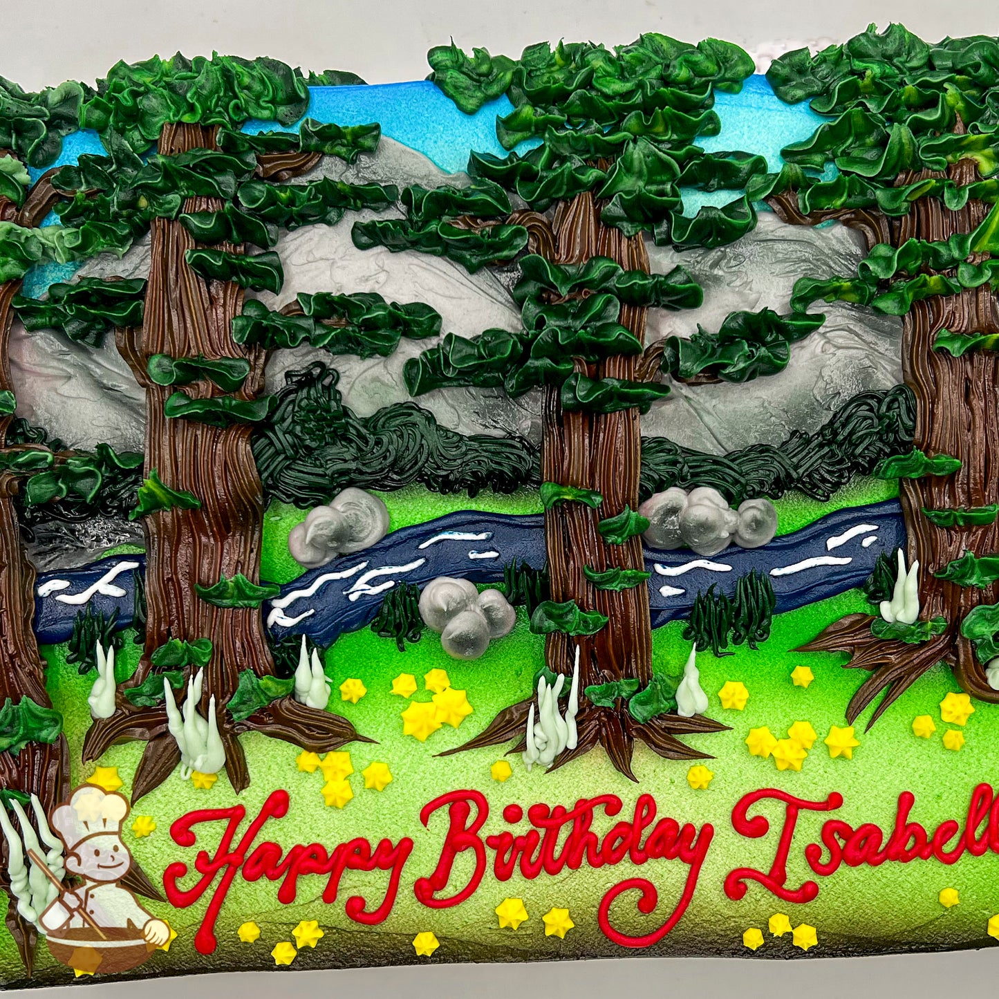 Sheet cake with buttercream redwood trees, river, mountains, and rocks. Yellow star-shaped flowers and green grass decorate the foreground.