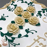 Sheet cake with buttercream decorations featuring a cross made of cream-colored roses and green leaves, surrounded by green vine designs and a cream border.