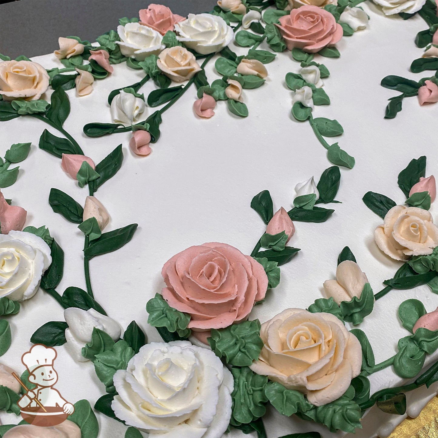 Sheet cake with buttercream decorations of pink, white, and peach roses, surrounded by green leaves and vines, creating a floral design.