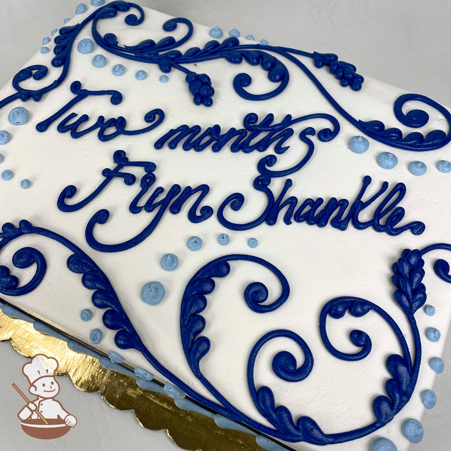 White sheet cake with blue buttercream scrollwork, floral accents, and small blue dots. 