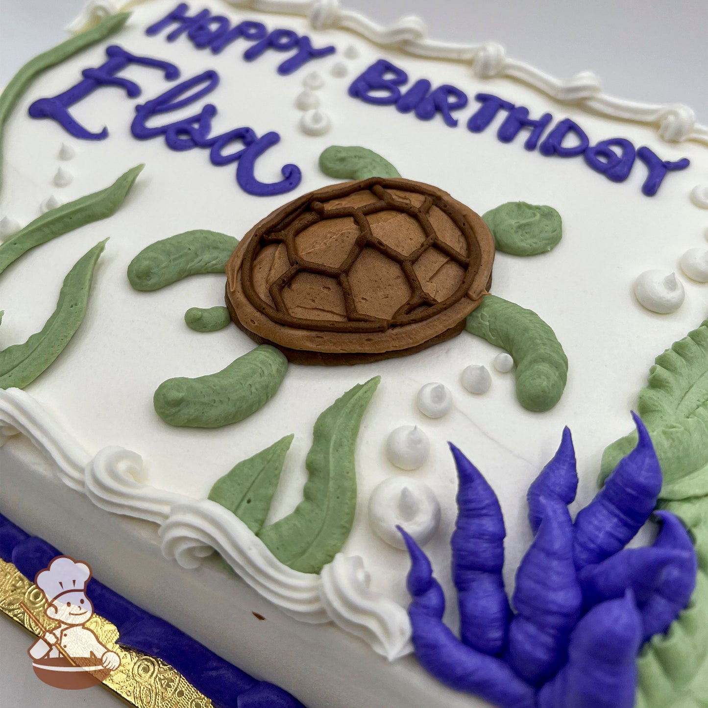 Sheet cake with buttercream sea turtle, green kelp, blue coral, and white bubble decorations on a white frosting base.