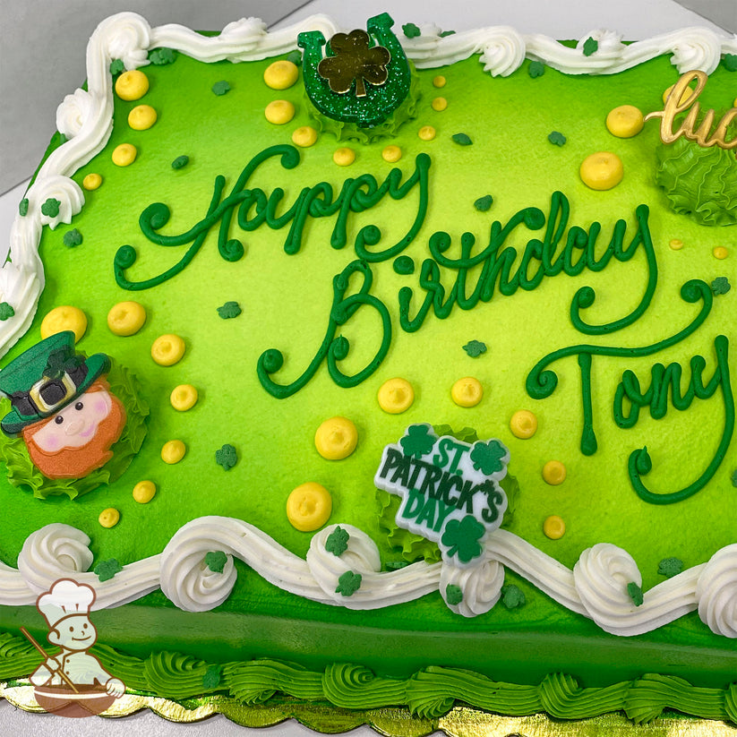 Green sheet cake with white buttercream swirl trims, shamrock sprinkles, yellow dots, a leprechaun face, a glittery horseshoe, and "St. Patrick's Day" plastic decorations.