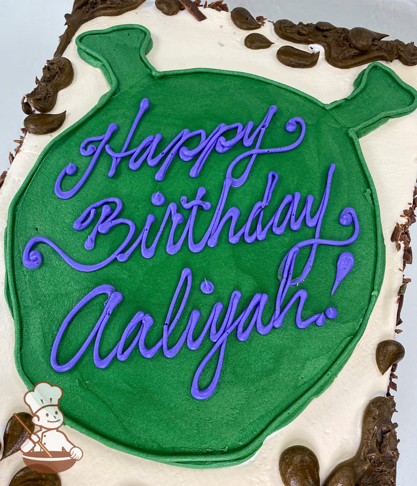 Sheet cake with white frosting, featuring a green Shrek head silhouette in the center. Brown frosting accents resemble mud around the edges.