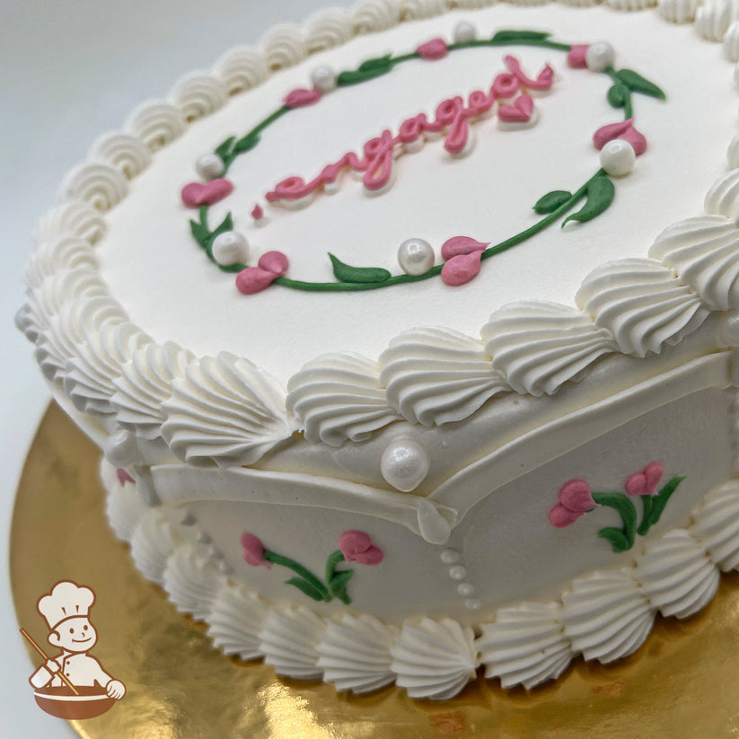 Round white cake, decorated with pink heart flower buds, green leaves, sugar pearls, and piped white frosting borders, on a gold base.