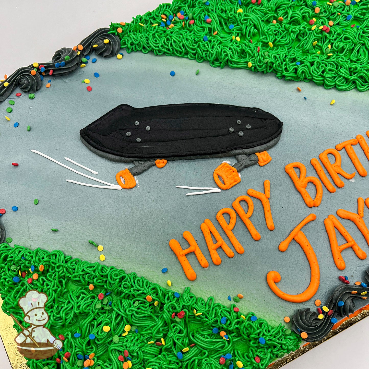 Sheet cake with buttercream skateboard decoration, surrounded by green grass-like icing and colorful sprinkles on a cement-colored background.