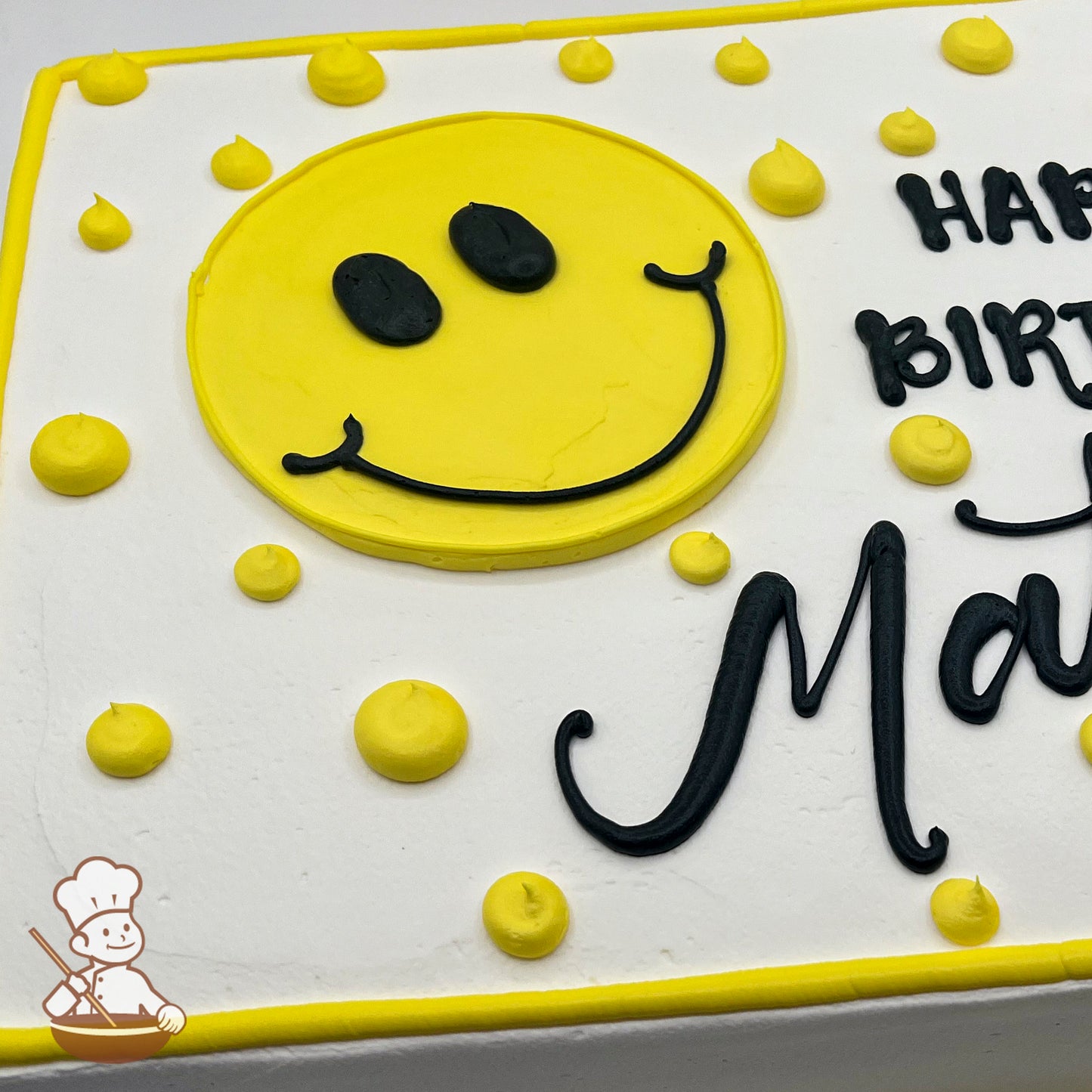 A sheet cake with white frosting, decorated with a large yellow buttercream smiley face and scattered yellow dots. Yellow border outlines the cake.