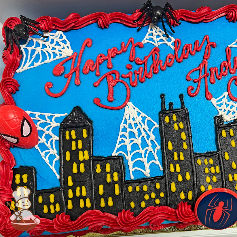 Sheet cake with a blue background, black city skyline with yellow windows, white buttercream spider webs, red border, and plastic spider decorations.