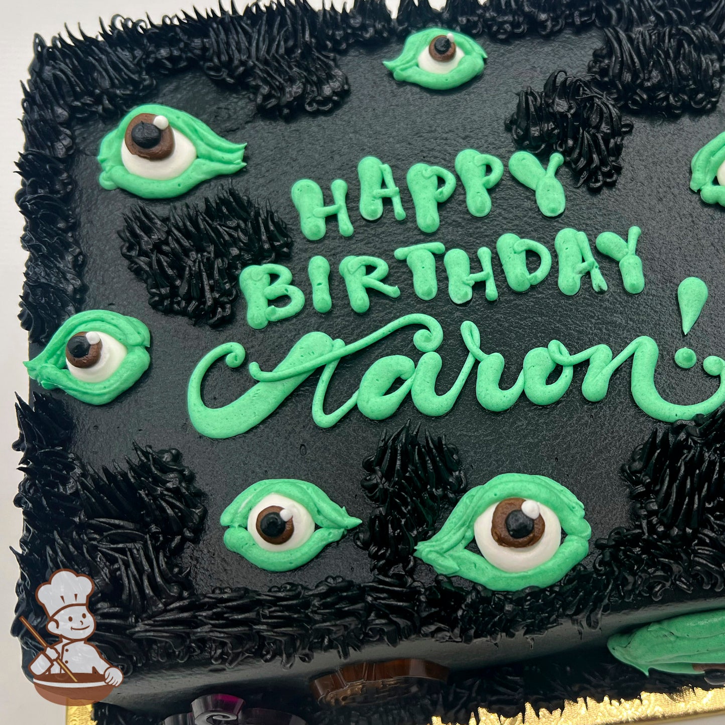 Black sheet cake with green buttercream spooky eyes and black textured buttercream accents resembling fur.