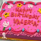 Pink sheet cake with buttercream stars, Piranha Plant decorations, and blue and pink dress trims.