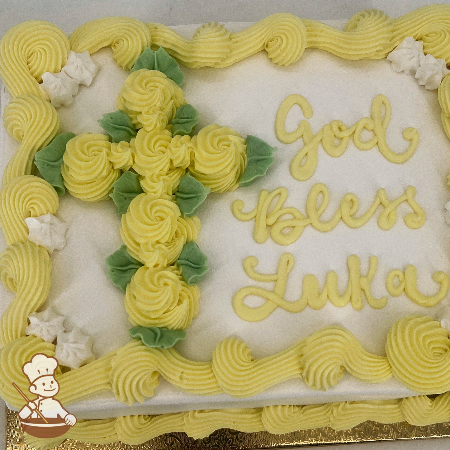 Sheet cake with yellow buttercream swirls forming a cross, accented by green leaves. Yellow piped borders and white star-shaped decorations.