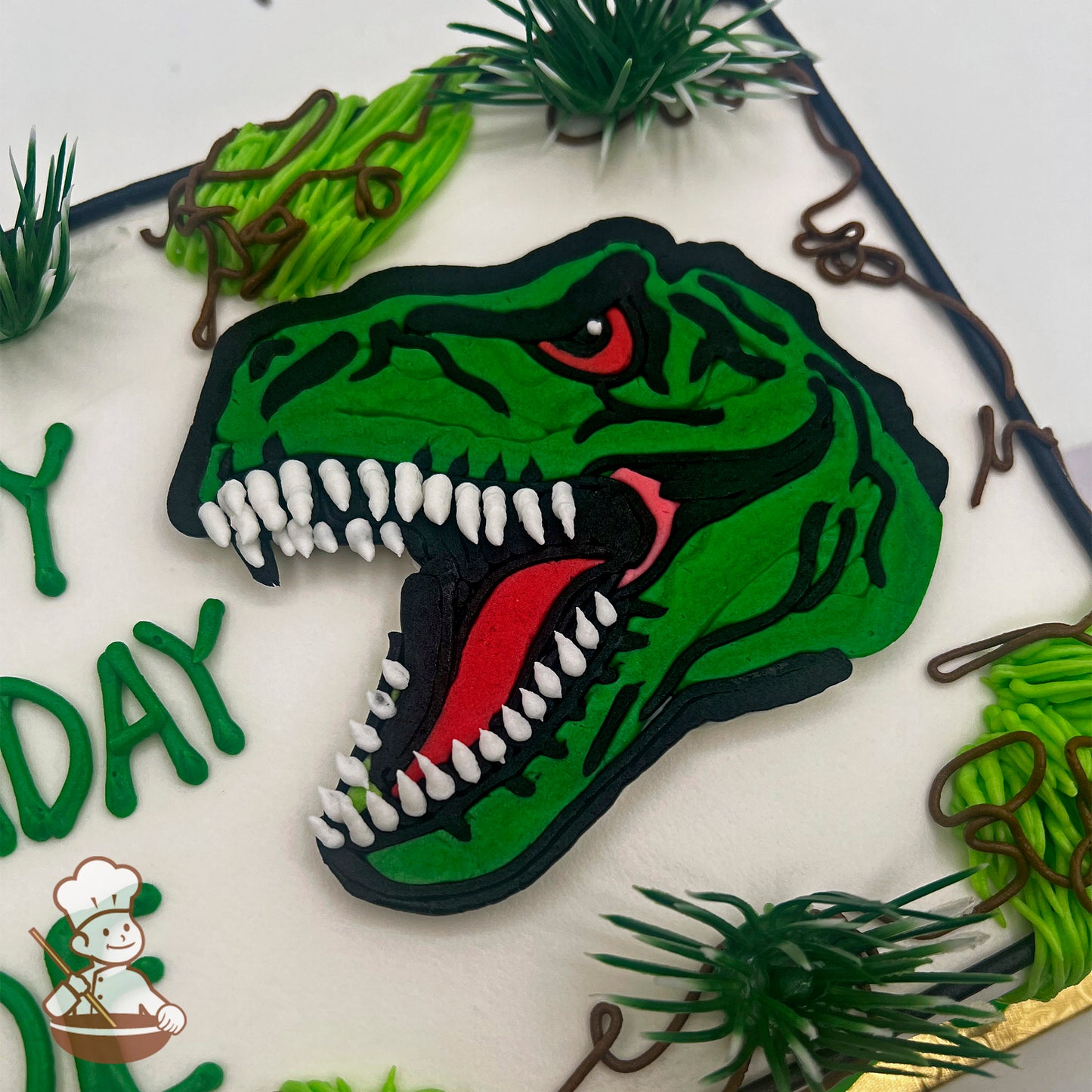 T-Rex head in green buttercream, roaring with white teeth, surrounded by plastic grass and brown vines on a sheet cake.