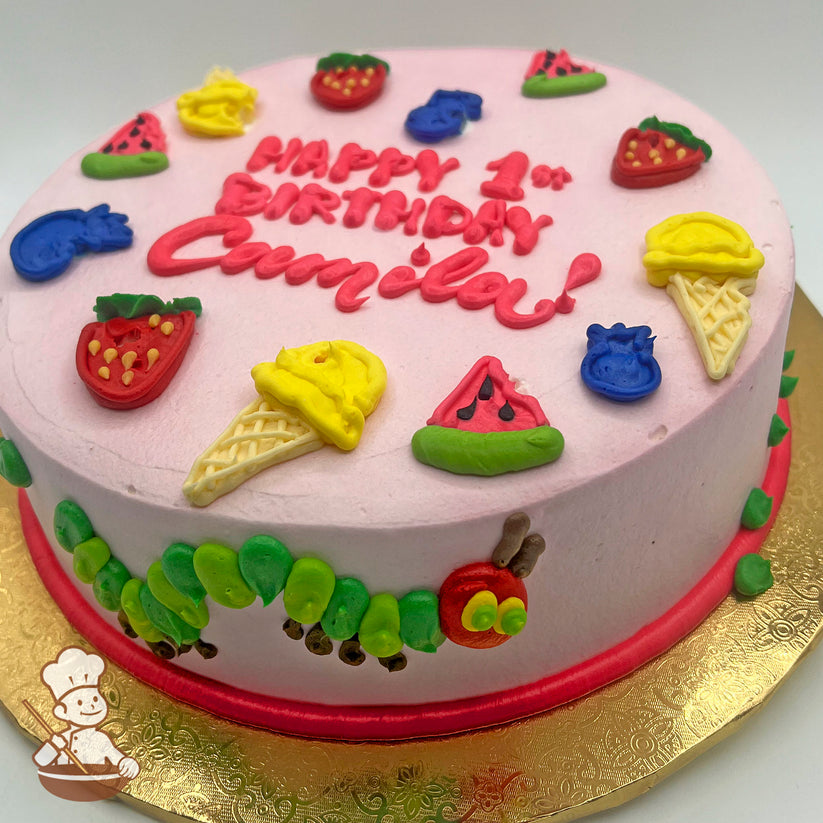 Round cake with pink icing, decorated with colorful fruits, ice cream cones, and a caterpillar design around the side.