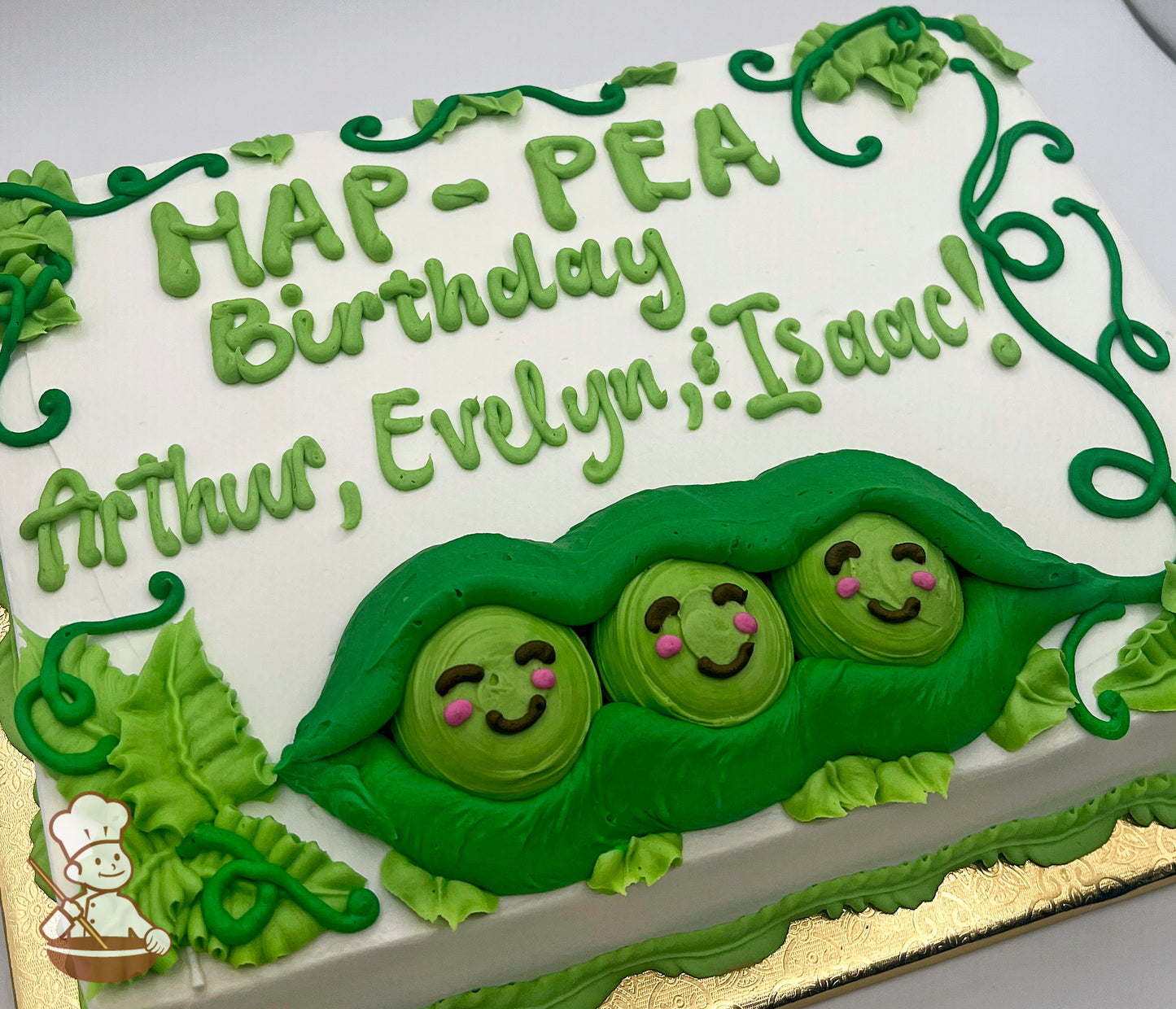 Sheet cake with buttercream decorations of three smiling peas in a green pod, surrounded by green leaves and vines.