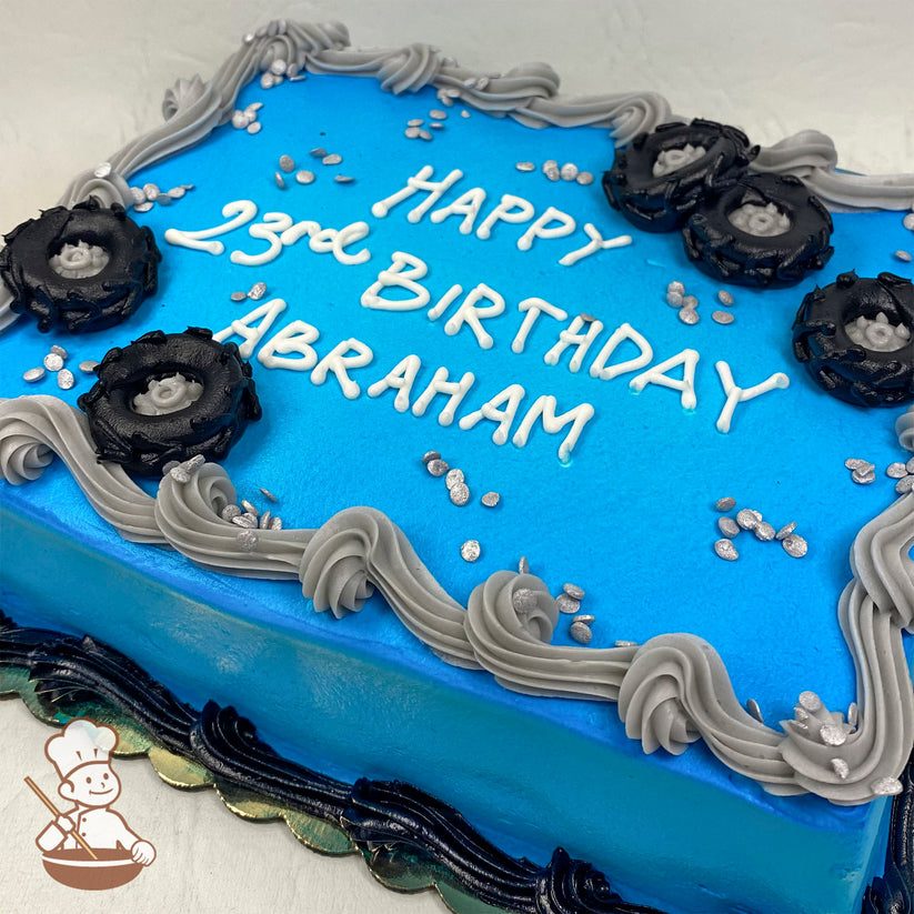 Blue sheet cake with gray buttercream swirls along the edges, black buttercream tire decorations, and silver sprinkle accents.