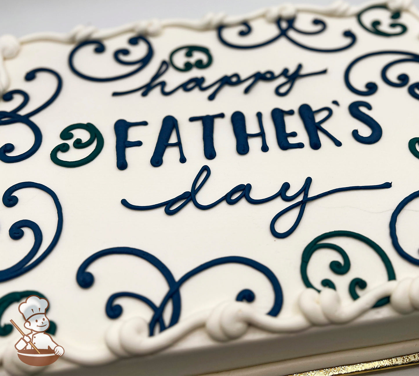 White sheet cake with blue and green buttercream scrolls, bordered with white piped edges.