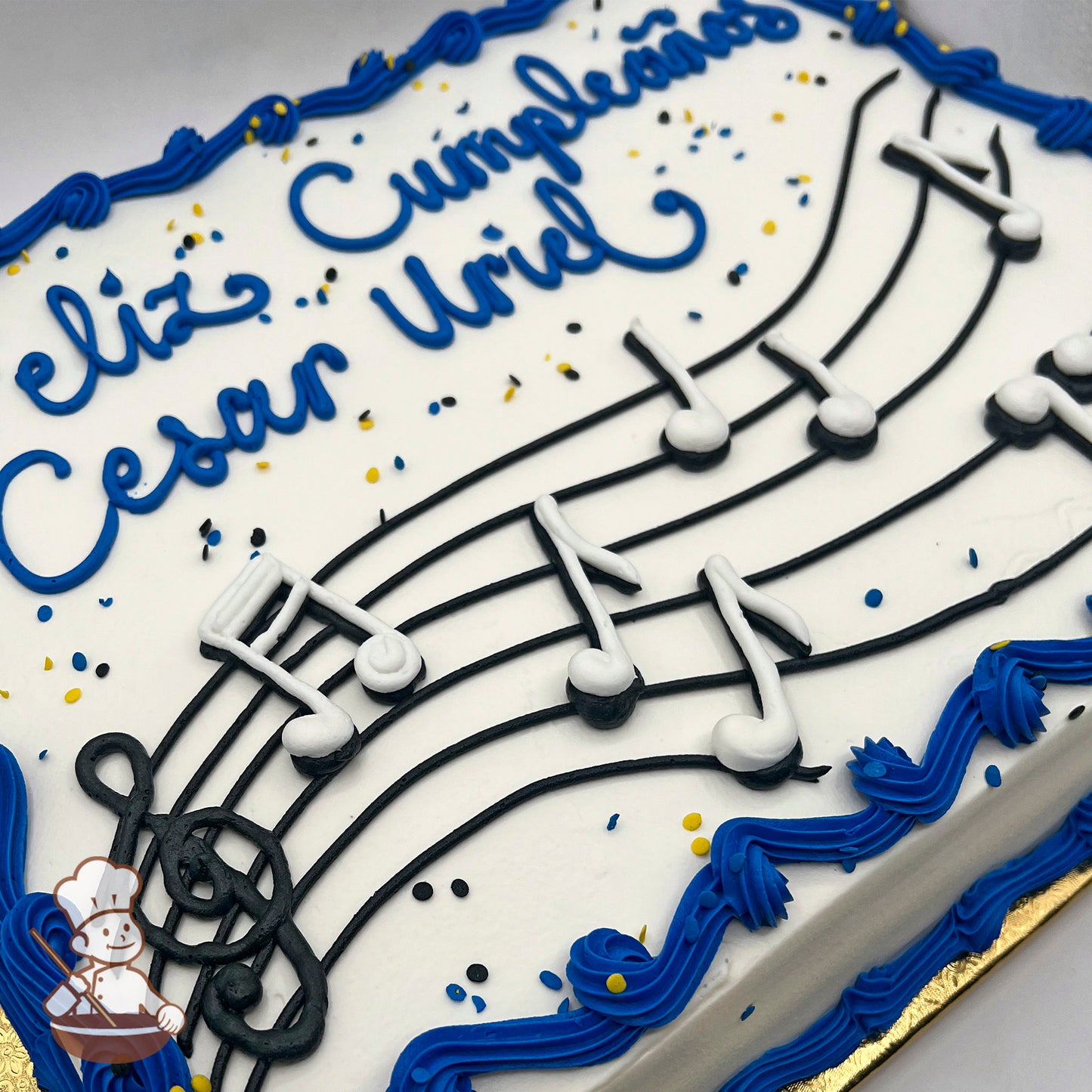 Sheet cake with white buttercream, decorated with black music staff lines, white and black music notes, blue piped borders, and yellow and black sprinkles.