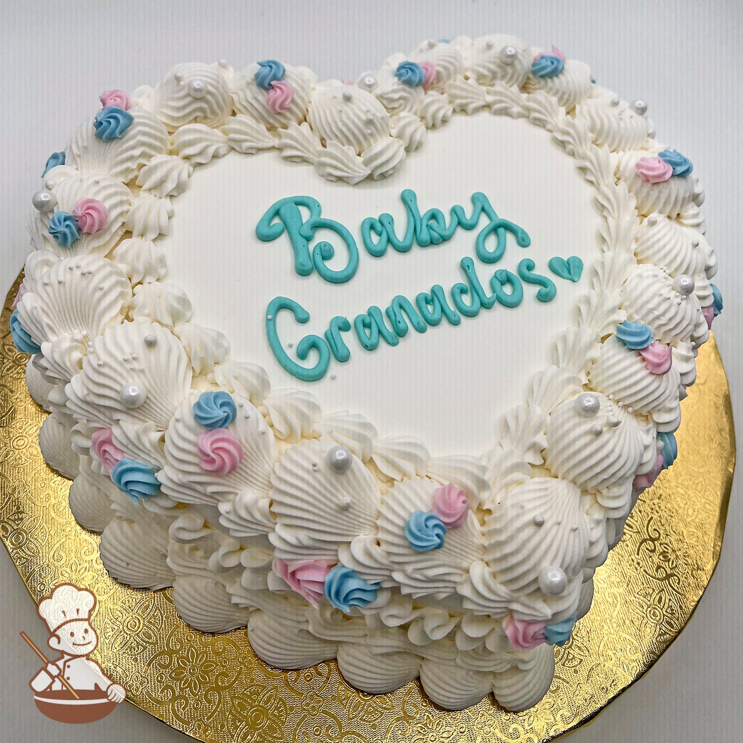 Heart-shaped sheet cake with white buttercream piping, rosettes in pink and blue, and white sugar pearls, displayed on a gold board.