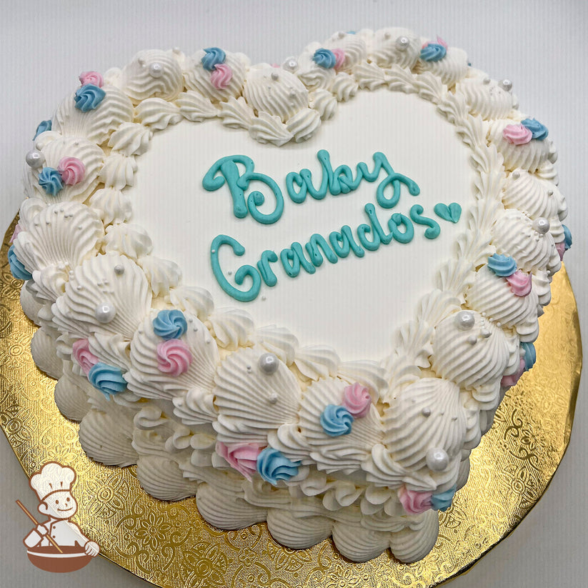 Heart-shaped sheet cake with white buttercream piping, rosettes in pink and blue, and white sugar pearls, displayed on a gold board.
