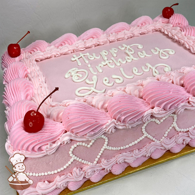 Pink sheet cake with piped buttercream hearts, vintage-style beading, maraschino cherries on corners, and decorative pink and white piping.