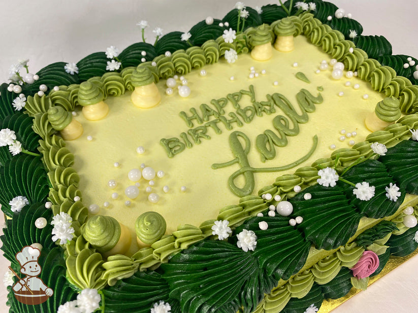 Sheet cake with green and yellow buttercream decorations, featuring piped grass, small white flowers, pearl sprinkles, and mushroom-shaped frosting accents.