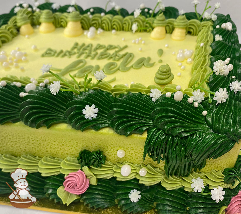 Sheet cake with green and yellow buttercream decorations, featuring piped grass, small white flowers, pearl sprinkles, and mushroom-shaped frosting accents.