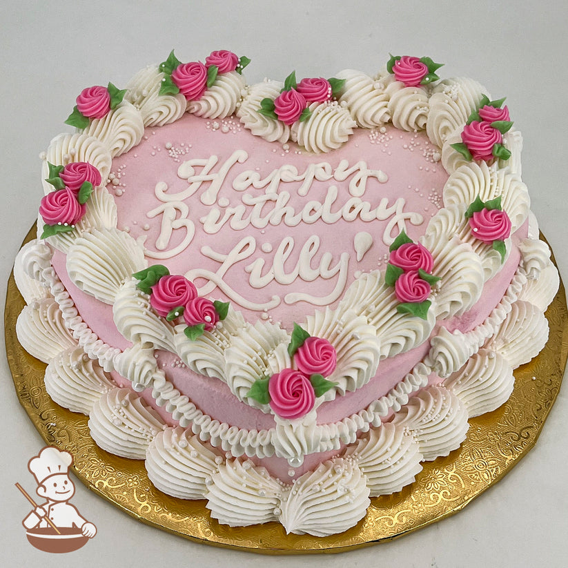 Heart-shaped pink sheet cake with vintage-style buttercream piping, pink swirlette buds, green leaves, and sugar pearls on a gold base.