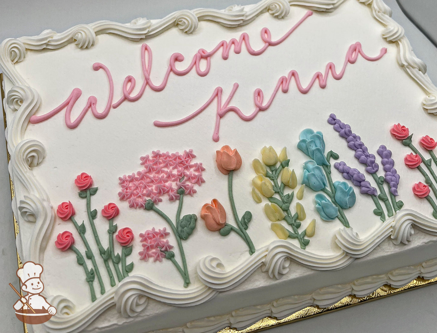 Sheet cake with white frosting, piped floral decorations including pink roses, pink hydrangeas, orange tulips, yellow and blue blossoms, and purple lavender.