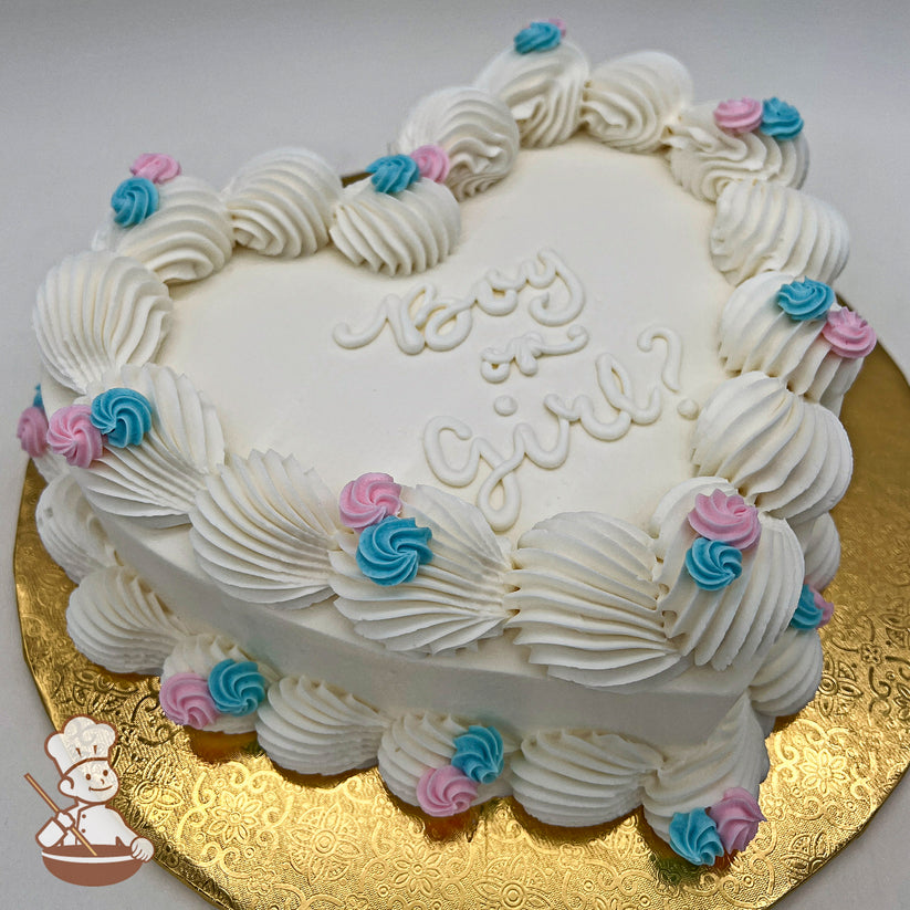 Heart-shaped white cake with wavy piped trim, decorated with pink and blue rosette flowers, on a gold embossed board.