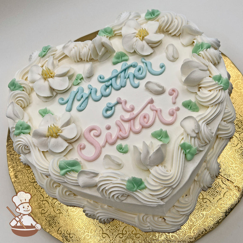 Heart-shaped cake with buttercream wavy trim, white blossoms, petals, and green leaves.